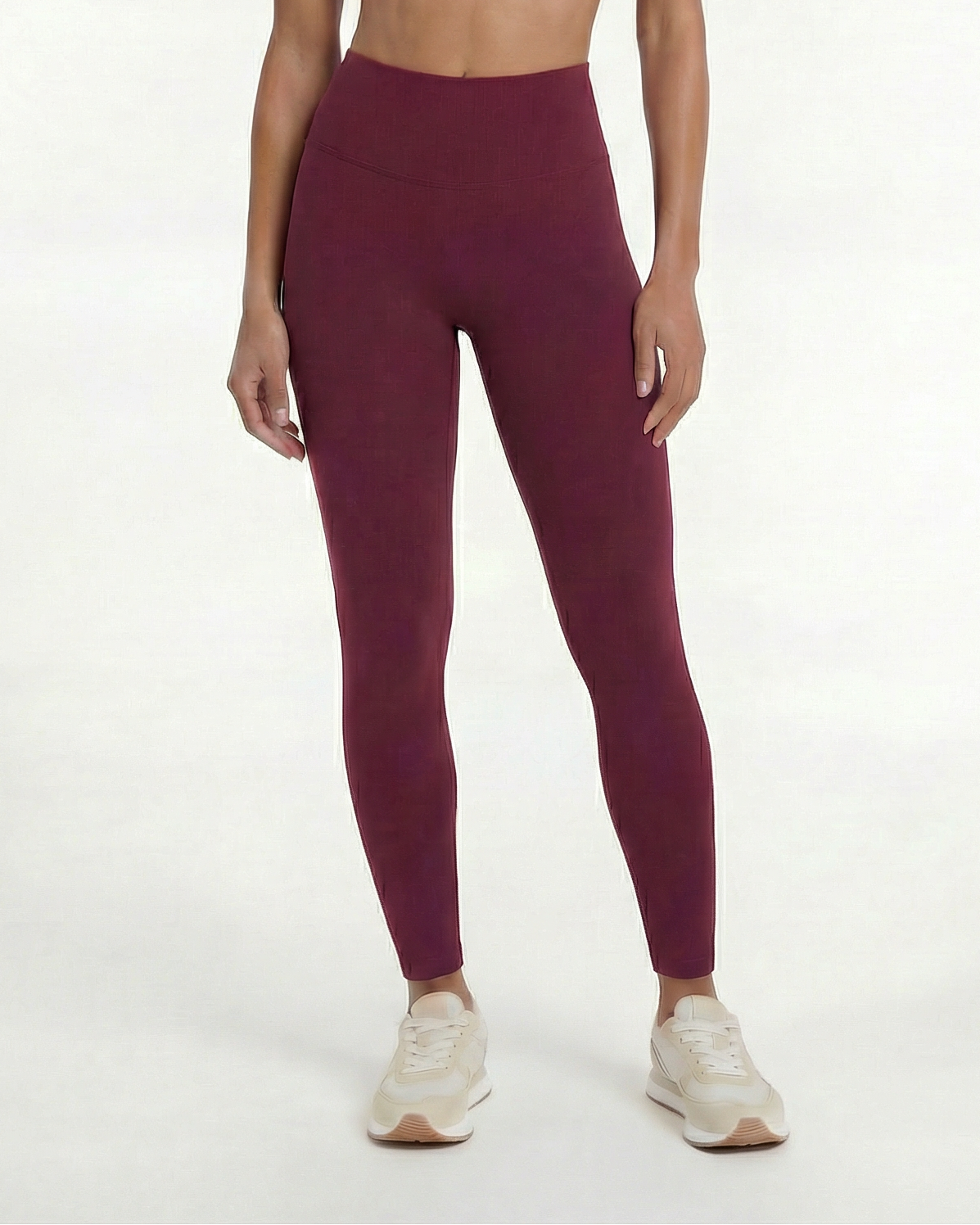 Woman wearing a maroon sports bra and leggings set on a white background