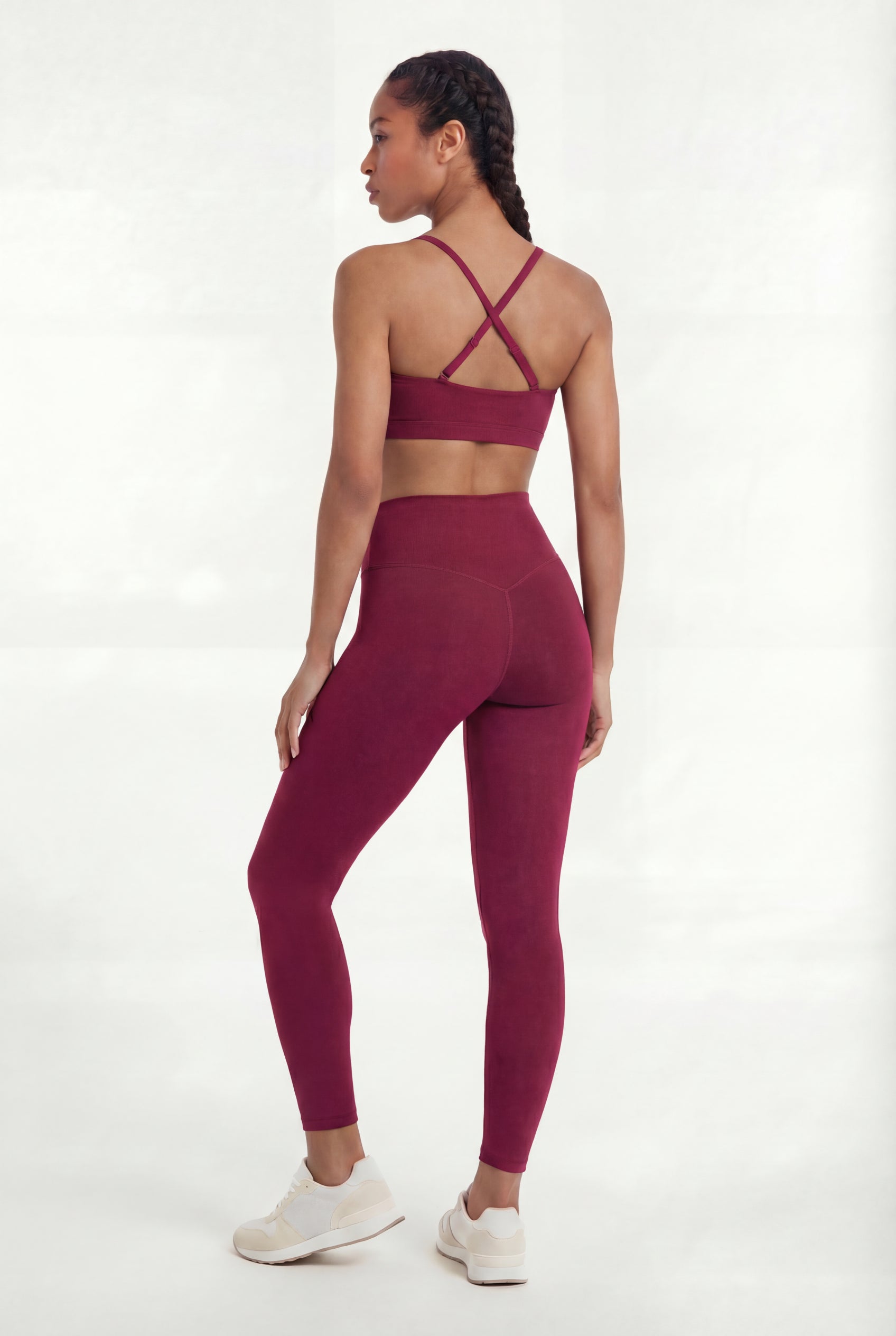 Woman wearing a maroon sports bra and leggings set on a white background