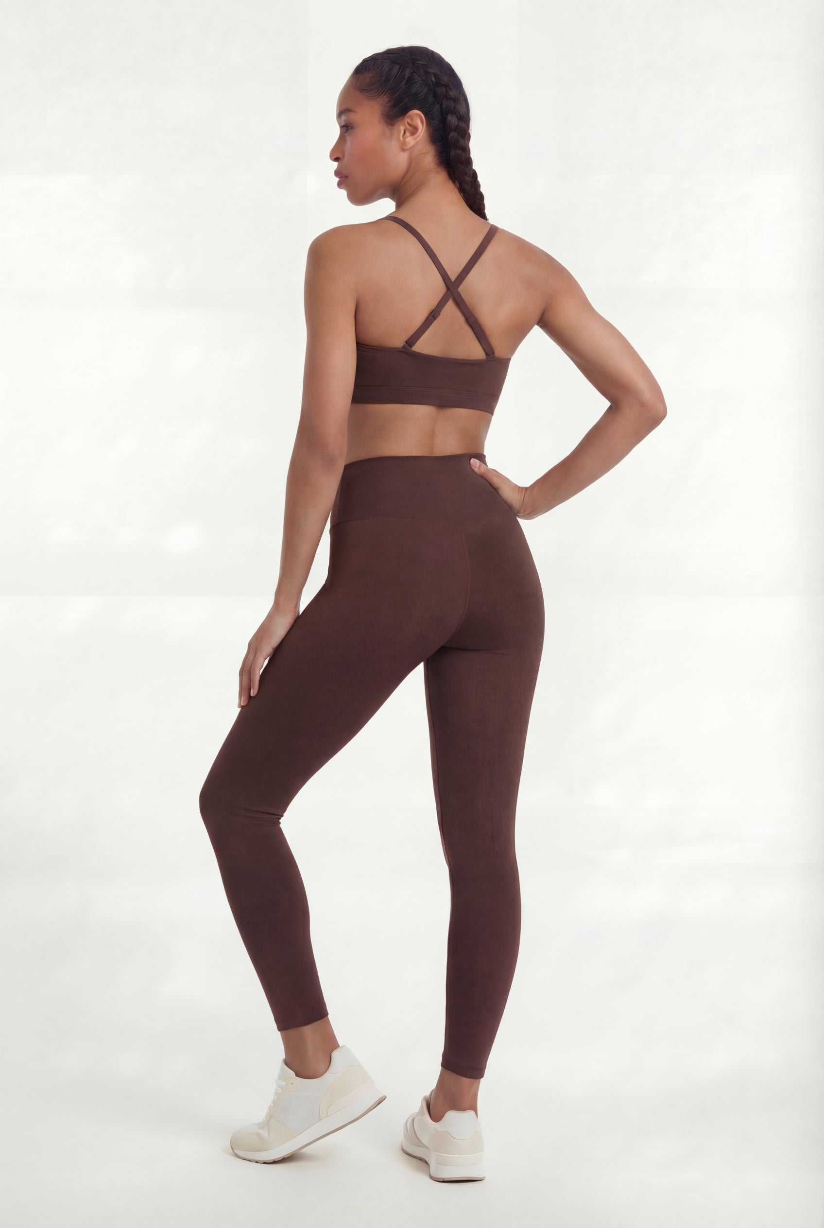 Woman wearing a brown sports bra and leggings set on a white background